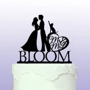 May include: Black silhouette cake topper featuring a bride and groom holding hands, a cat, and a heart with the text "Mr. & Mrs." and the word "BLOOM" below.