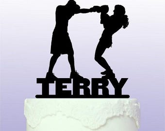 May include: Black silhouette of a couple boxing with the name "TERRY" written below them. This is a cake topper.
