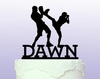 May include: Black silhouette of two people boxing with the word "DAWN" underneath. The silhouette is on top of a white cake.