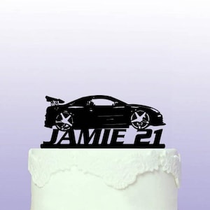 May include: Black silhouette of a car with the name Jamie and the number 21 on a white cake.
