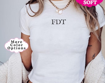 Op de afbeelding: Wit gecropped T-shirt met de tekst "FDT" in zwarte letters. Het shirt is superzacht en heeft een ontspannen pasvorm.
