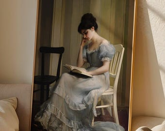 Può includere: Una stampa artistica incorniciata con un dipinto classico di una donna in un abito azzurro che legge un libro. L'opera d'arte è esposta su un divano beige con cuscini e una coperta, creando un'atmosfera accogliente ed elegante.