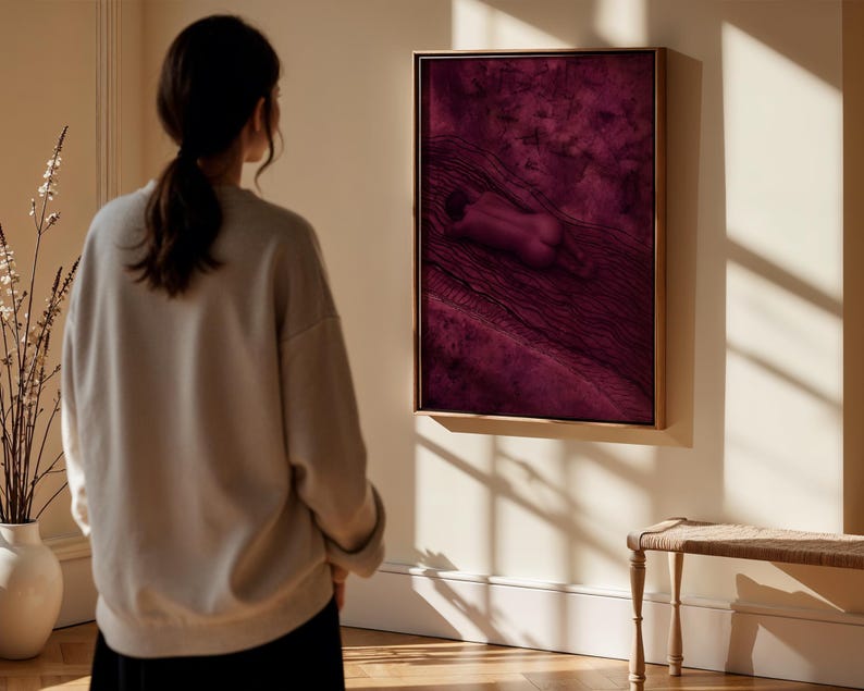 Op de afbeelding: Een rechthoekig wandkunstwerk met een diep magenta en donkerpaarse monochrome sc&egrave;ne van een figuur die op een getextureerd oppervlak ligt. Het kunstwerk is ingelijst in een dunne, lichtgekleurde houten lijst en hangt aan een lichte muur.