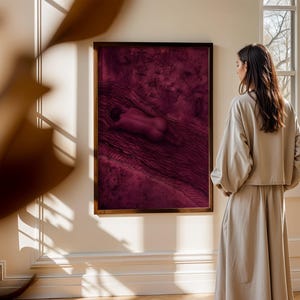 Op de afbeelding: Een rechthoekig wandkunstwerk met een abstracte compositie in diep magenta en donkerpaars met een centrale liggende figuur, gevat in een dunne donkerbruine lijst en opgehangen aan een lichtgekleurde muur.