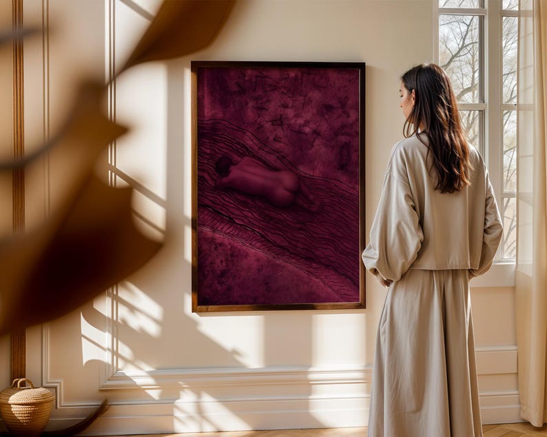 Op de afbeelding: Een rechthoekig wandkunstwerk met een abstracte compositie in diep magenta en donkerpaars met een centrale liggende figuur, gevat in een dunne donkerbruine lijst en opgehangen aan een lichtgekleurde muur.