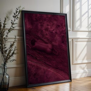 Op de afbeelding: Een ingelijste verticale kunstprint met een diep bordeauxrode en kastanjebruine kleurenpalet. Het kunstwerk toont een menselijk figuur liggend op een gestructureerd oppervlak met donkere, golvende lijnpatronen en abstracte vormen.