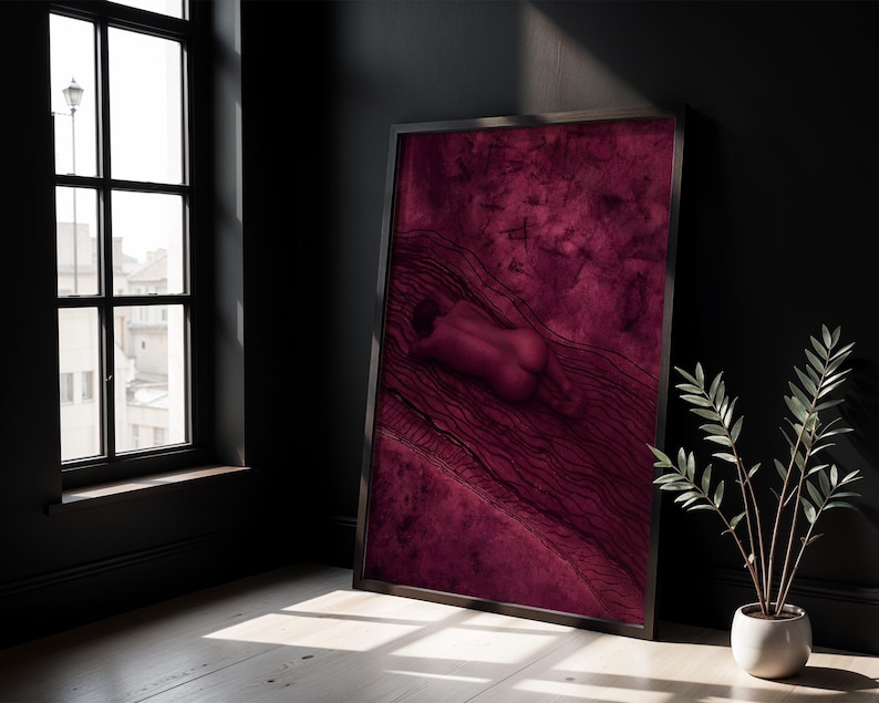 Op de afbeelding: Een ingelijste verticale wandkunstprint met een diep magenta en donkerrode monochrome illustratie van een menselijk figuur dat op een getextureerd oppervlak ligt met golvende lijnpatronen en verspreide donkere markeringen.
