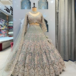 Op de afbeelding: Een groene en gouden geborduurde lehenga met een bijpassende choli en dupatta. De lehenga heeft ingewikkelde bloemen- en pauwenmotieven en is versierd met pailletten en kralen.