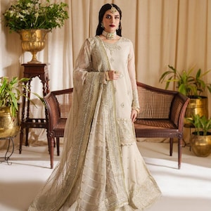 May include: A white bridal outfit with intricate silver embroidery and embellishments. The outfit includes a long-sleeved top, a flowing skirt, and a matching dupatta.