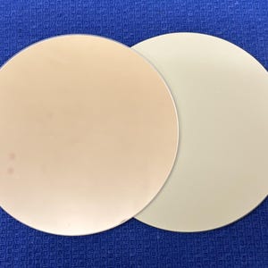 Może przedstawiać: Dwa okrągłe talerze ceramiczne, jeden jest jasnobeżowy, a drugi jasnokremowy.