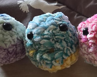 May include: Eight colorful crocheted plush toys with googly eyes. The toys are in shades of purple, blue, pink, yellow, and white.