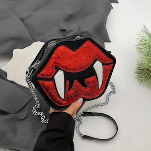 May include: A black crossbody bag with a red glitter vampire mouth design and a silver chain strap.