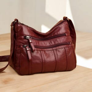 May include: A burgundy faux leather shoulder bag with multiple zippered compartments and a long adjustable strap.