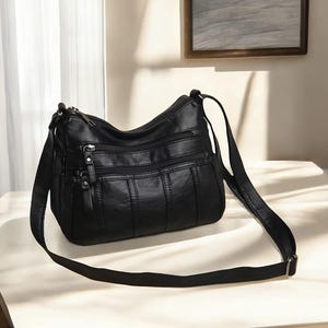 May include: A black leather shoulder bag with multiple pockets and a zipper closure. The bag has a long adjustable strap.