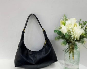 May include: A black leather handbag with a curved shape and a single strap. The bag has a gold-toned zipper closure.