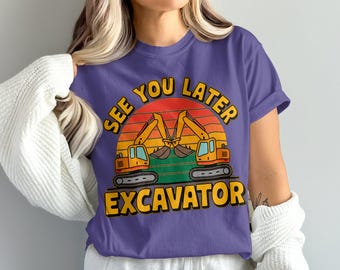 Può includere: T-shirt viola con grafica di due escavatori gialli su un design a tramonto. Il testo "SEE YOU LATER" è arcuato sopra gli escavatori e "EXCAVATOR" è stampato sotto. Un capo d'abbigliamento casual.