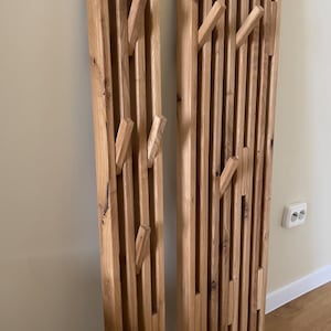 May include: Two tall, vertical wall-mounted coat racks constructed from light brown natural wood slats. Each rack features multiple integrated, angled wooden pegs extending outward from the slatted surface, designed for hanging items.