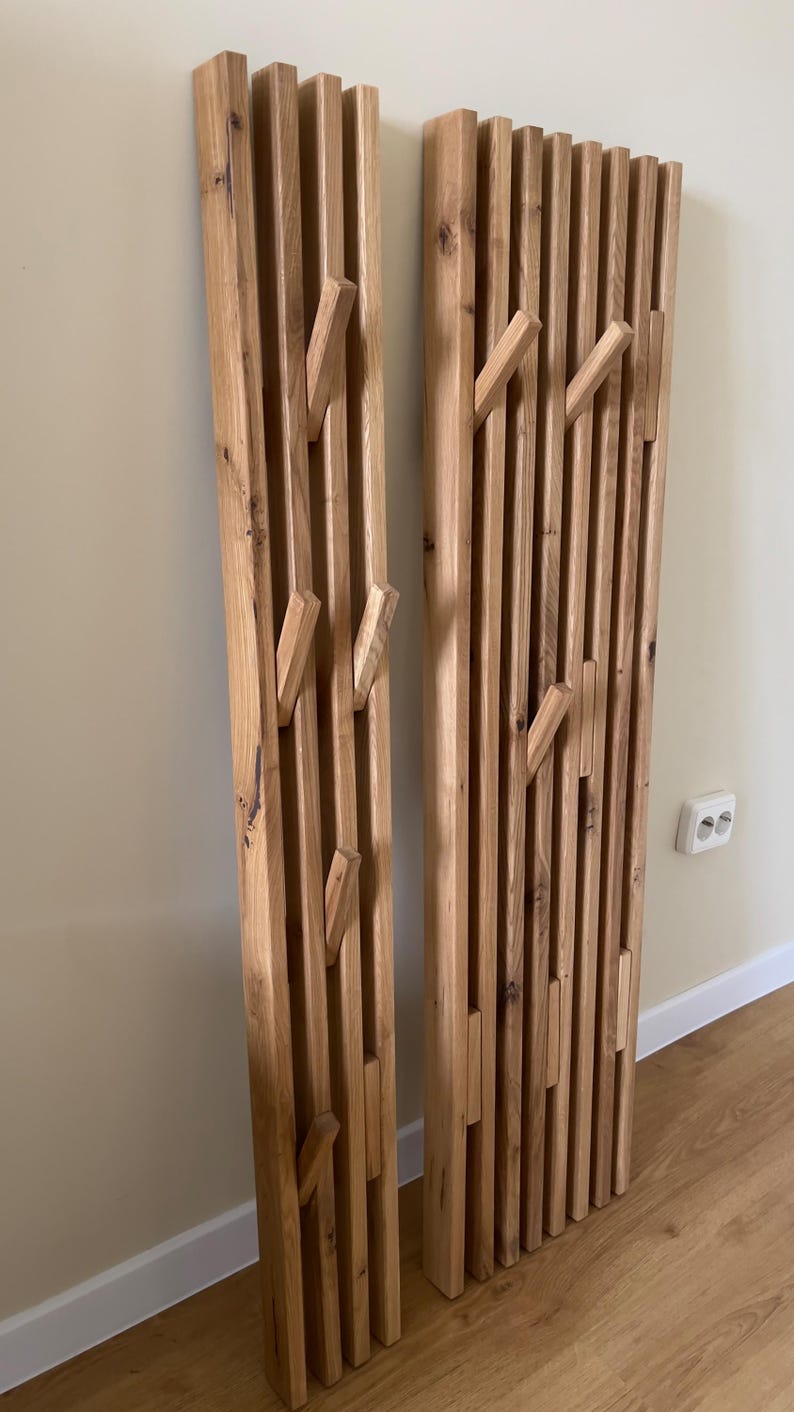May include: Two tall, vertical wall-mounted coat racks constructed from light brown natural wood slats. Each rack features multiple integrated, angled wooden pegs extending outward from the slatted surface, designed for hanging items.