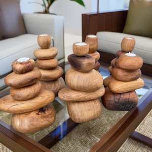 May include: Three wooden candle holders, each stacked with five round pieces of wood, resembling a zen rock garden. The candle holders are arranged on a glass table top.
