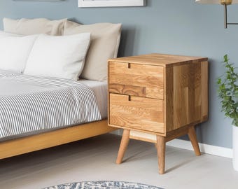 May include: A wooden nightstand with two drawers and a light wood finish. The nightstand has four legs and is sitting next to a bed with a striped comforter.