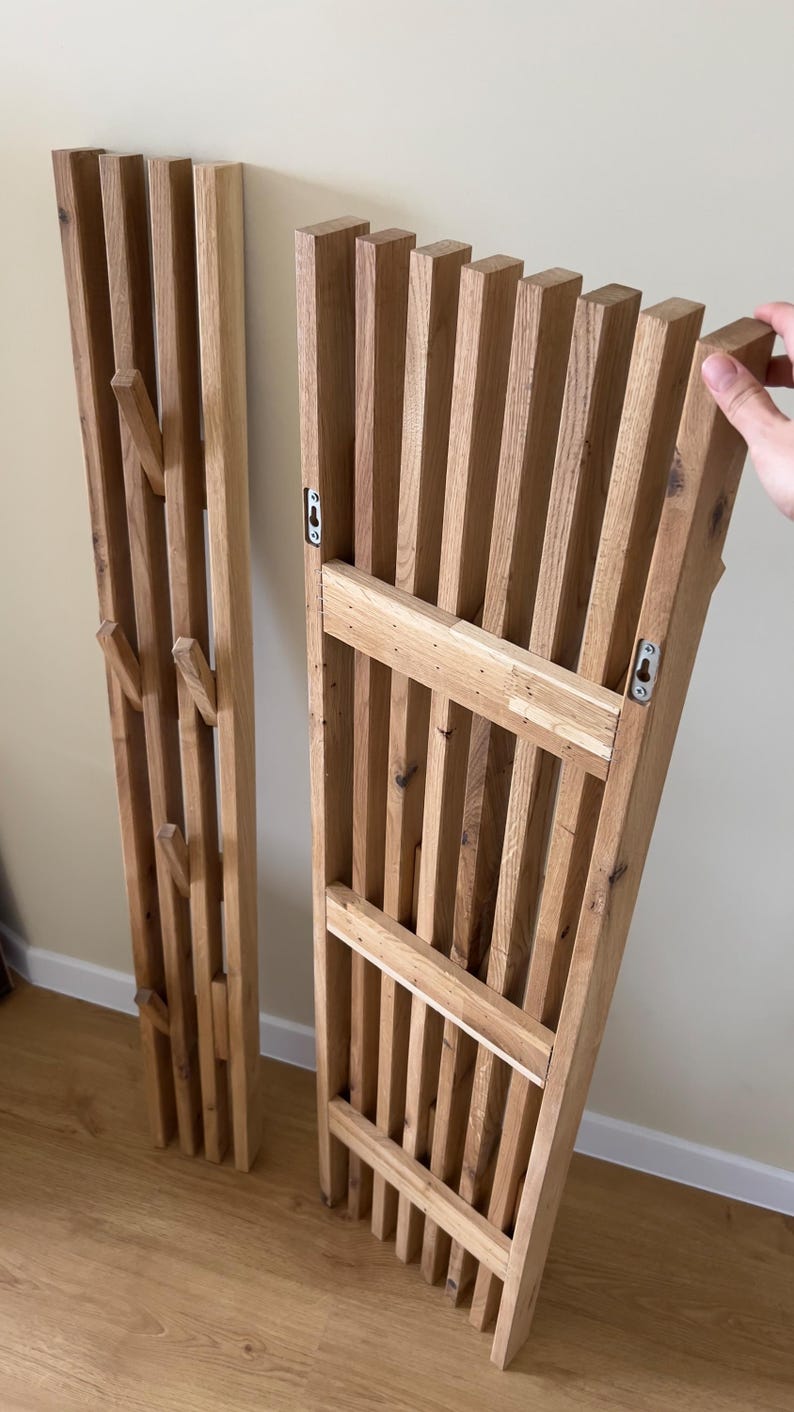 May include: Two vertical wall-mounted coat racks made of light-toned wood. Each rack features a slatted design with multiple protruding wooden pegs for hanging items. The back of the rack shows metal keyhole mounting hardware for installation.