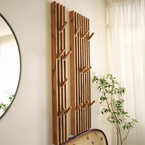 May include: Two wooden wall-mounted coat racks with a slatted design and angled hooks. The racks are made of natural wood with a light brown finish.