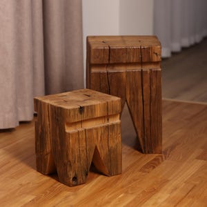 May include: Two wooden stools with a rustic, reclaimed wood design. The stools are made of thick, rough-hewn planks with visible knots and grain patterns. The larger stool is taller than the smaller stool.