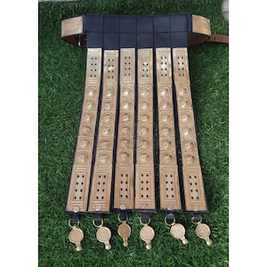 May include: A black leather Roman military belt with gold-colored metal accents. The belt has six rows of round metal studs and a decorative design on the top.