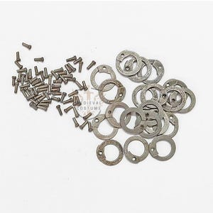 May include: A selection of small, antique-style metal rivets and circular fasteners. The rivets are cylindrical with rounded heads, while the fasteners are ring-shaped with a split and two holes. The items are scattered on a white surface.