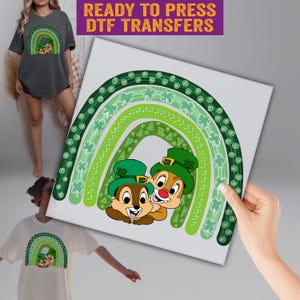 May include: A white square featuring a green rainbow design with shamrocks and two cartoon chipmunks wearing green leprechaun hats. The text "READY TO PRESS DTF TRANSFERS" is at the top. The design is also shown on a t-shirt.