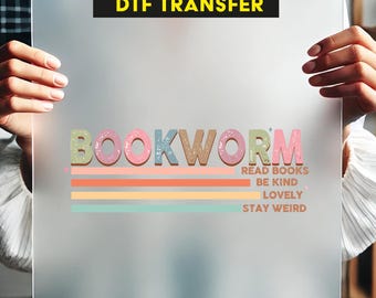May include: Ready to press DTF transfer with the text "BOOKWORM" in pink, green, and blue letters with a glittery texture. The text is layered over a rainbow of pastel stripes with the text "READ BOOKS, BE KIND, LOVELY, STAY WEIRD" underneath.