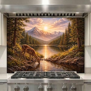 May include: A kitchen backsplash panel featuring a landscape print of a deer drinking from a lake at sunset, surrounded by pine trees and snow-capped mountains. The panel is installed behind a stainless steel gas stove and range hood.