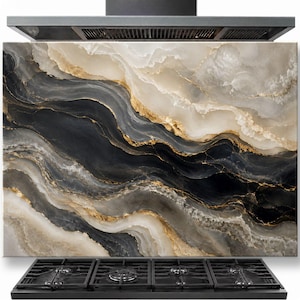 Puede incluir: Un panel rectangular para salpicadero de cocina con un patrón de mármol de ondas fluidas en tonos negros, crema y blancos, acentuado por finas vetas doradas. El panel está colocado verticalmente detrás de una estufa de gas negra de cuatro quemadores.