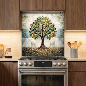 May include: A kitchen backsplash mural featuring a stylized tree with vibrant green and gold leaves set against a light blue marble-patterned tile background, positioned directly behind a stainless steel gas stove with black burner grates.