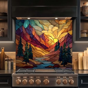 Puede incluir: Un panel para salpicadero de cocina con una ilustración de paisaje estilo vidriera que muestra una cordillera, un río y árboles de hoja perenne bajo un cielo al atardecer con tonos vibrantes de naranja, amarillo, morado y azul.