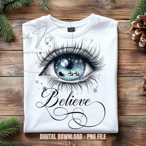 Könnte beinhalten: Weißes T-Shirt mit einem detaillierten Augendesign. Die Iris zeigt eine Winterszene mit dem Schlitten des Weihnachtsmanns und Rentieren. Das Wort "Believe" ist in Schrift unter dem Auge geschrieben. Der Satz "DIGITAL DOWNLOAD - PNG FILE" ist ebenfalls vorhanden.