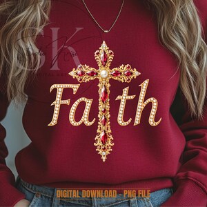 Puede incluir: Una sudadera granate con una cruz enjoyada dorada y roja con la palabra "Faith" en letras doradas. La cruz está adornada con piedras preciosas rojas y una perla central. Se ve un delicado collar de oro.