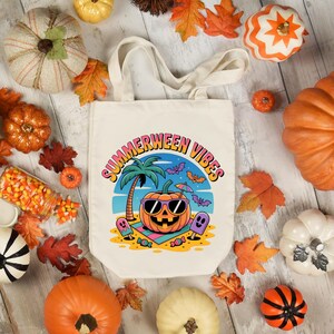May include: Cream-colored tote bag with the text "Summerween Vibes" and a graphic of a pumpkin wearing sunglasses on a beach. The image is surrounded by pumpkins, fall leaves, and candy corn.