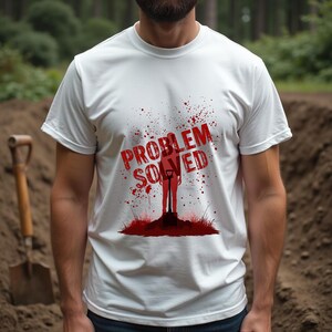 May include: White t-shirt with a red graphic. The design includes the words "PROBLEM SOLVED", a silhouette of a person with a shovel, and red splatter effects. The shirt is short-sleeved.