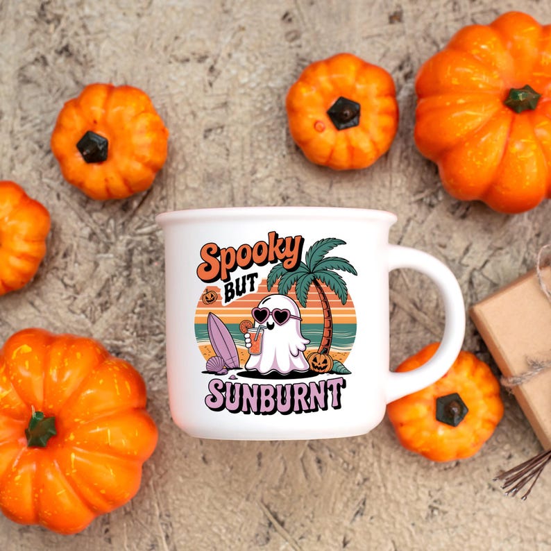 May include: White enamel mug with a Halloween-themed design. The mug features the text "Spooky BUT Sunburnt" with a cartoon ghost wearing sunglasses, a surfboard, and a tropical beach scene. Surrounding the mug are several orange pumpkins.