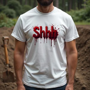Pu&ograve; includere: T-shirt bianca con la scritta "Shhh" in rosso, con un design a gocce simile a sangue. La maglietta &egrave; a maniche corte e girocollo. Sullo sfondo, una pala e un cumulo di terra.