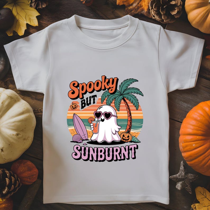 May include: White t-shirt with a colorful graphic featuring a ghost wearing heart-shaped sunglasses, holding a drink, and standing on a beach with a palm tree. The text "Spooky BUT Sunburnt" is above and below the graphic.