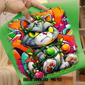 May include: A digital graphic of a grumpy gray cat with yellow eyes, decorated with Christmas ornaments and vines, set against a vibrant graffiti background. The cat is on a green background with the text "DIGITAL DOWNLOAD - PNG FILE".