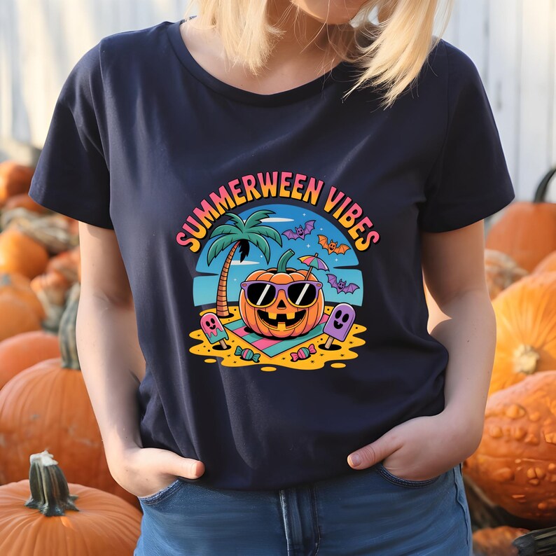 May include: Navy blue t-shirt with a colorful graphic that says "Summerween Vibes." The graphic features a smiling pumpkin wearing sunglasses on a beach with a palm tree, bats, and ghosts. The shirt is surrounded by pumpkins.