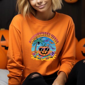 May include: Orange long-sleeve sweatshirt with a graphic that says "Summerween Vibes." The graphic features a pumpkin wearing sunglasses on a beach with a palm tree, bats, and ghosts. The sweatshirt is a solid orange color.