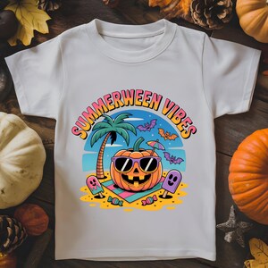 May include: White t-shirt with a colorful graphic that says "Summerween Vibes." The design features a smiling jack-o'-lantern wearing sunglasses on a beach, with palm trees, bats, and ice cream. The shirt is made of a soft material.