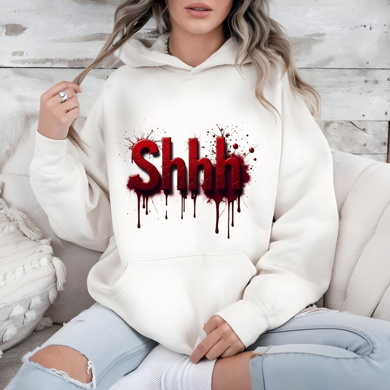 Pu&ograve; includere: Felpa con cappuccio color crema con la scritta "Shhh" in lettere rosse con effetto gocciolante di sangue. La grafica &egrave; circondata da schizzi rossi. La felpa ha una tasca frontale e un cappuccio con coulisse.