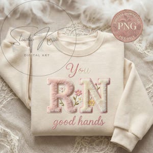 Op de afbeelding: Crèmekleurige sweatshirt met de geborduurde tekst "You RN good hands" in roze script. De letters "RN" zijn in een pluche, getextureerde stijl, met kleine bloemaccenten. Het ontwerp bevat een "DIGITAL DOWNLOAD PNG FILE ONLY" afbeelding.