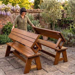 May include: A convertible wooden bench that transforms into a picnic table with two attached benches. The furniture is made of stained brown wood with a smooth finish and features a rectangular metal plaque on the lower side support frame.
