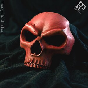 May include: A red skull mask with large eye sockets and a detailed jawline. The mask is made of a textured material and is set against a dark background. The Incognito Studios logo is visible in the upper right corner.